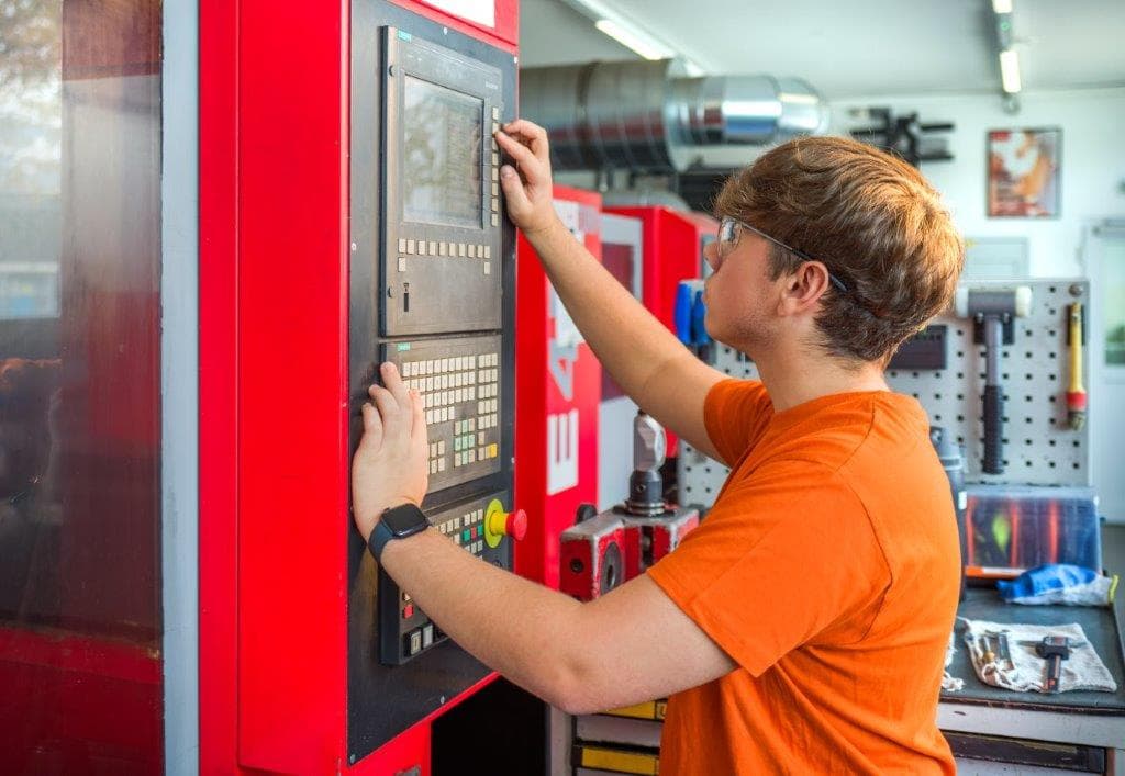 Lehrling bedient die Steuerung einer CNC-Maschine