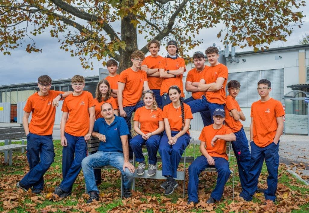 Die Lehrlinge der Flowserve Lehrwerkstätte mit ihrem Ausbilder unter einem Baum vor dem Werk