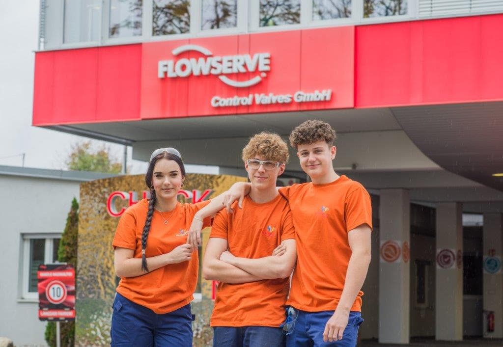Drei Lehrlinge in orangen Flowserve-Shirts vor dem Werk in Villach